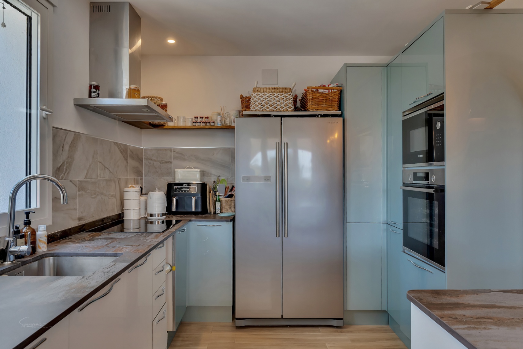 Cocina con encimeras de piedra, electrodomésticos de acero inoxidable y gabinetes azul pálido.