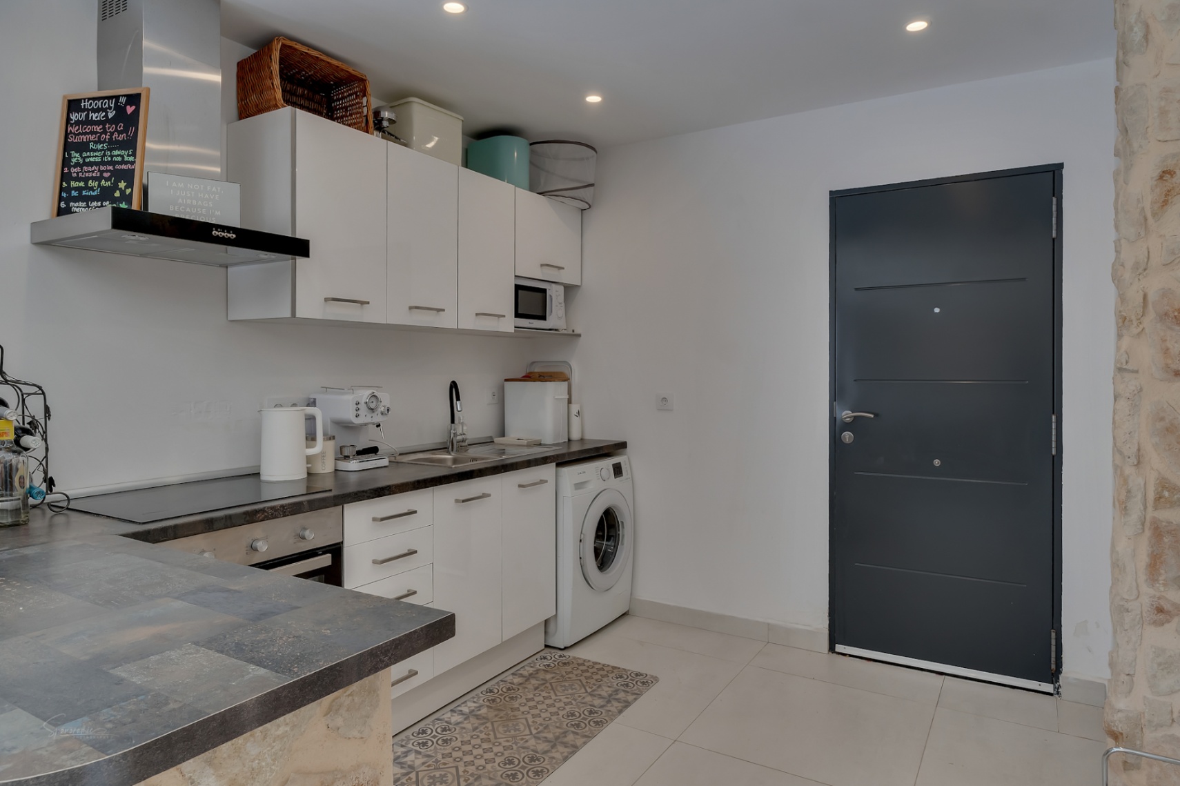 Cocina funcional con encimera oscura, armarios blancos y electrodomésticos modernos. Incluye lavadora y puerta de acceso.