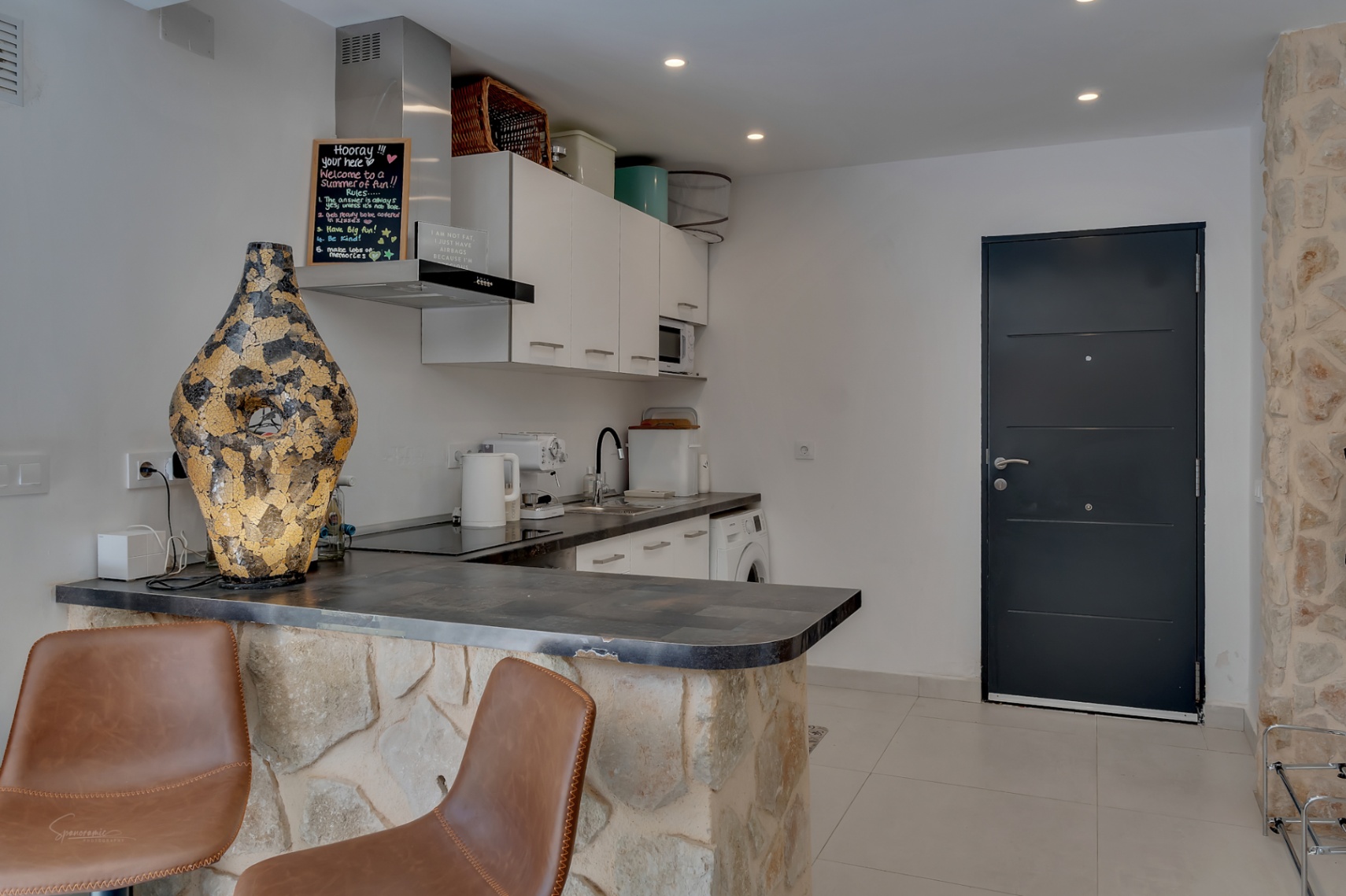 Detalle de la cocina con barra de piedra y sillas de cuero marrón, bajo iluminación empotrada.