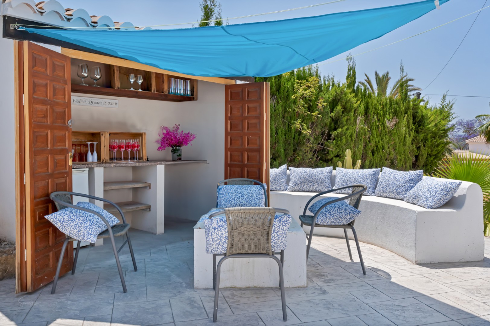 Detalle de la terraza con barra exterior, toldo azul y asientos con cojines estampados.
