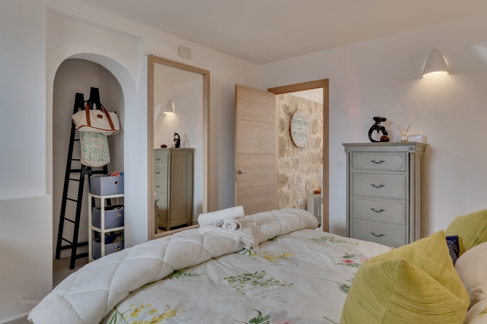 Detalle del dormitorio con nicho decorativo, cómoda gris y ropa de cama floral.