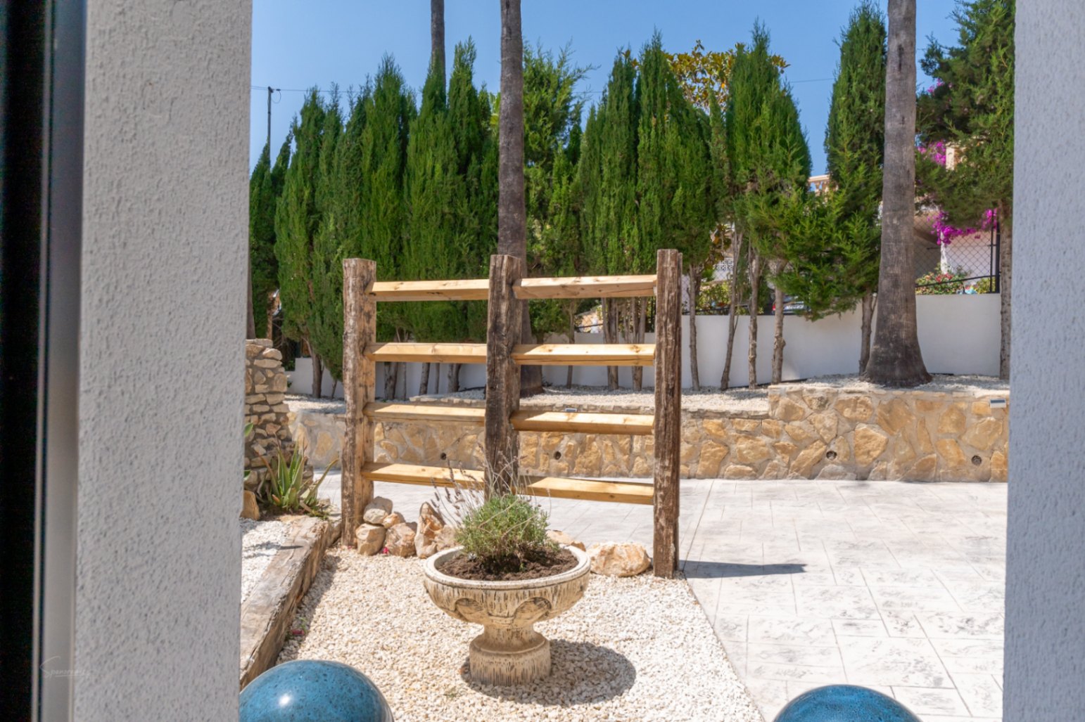 Detalle del jardín con estantería rústica de madera y maceta ornamental en Jávea.