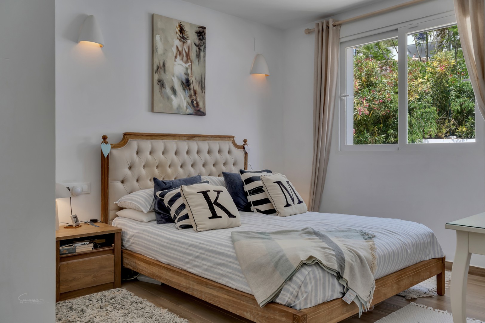 Dormitorio luminoso con cama de madera y cabecero tapizado. Decoración neutra y luz natural.