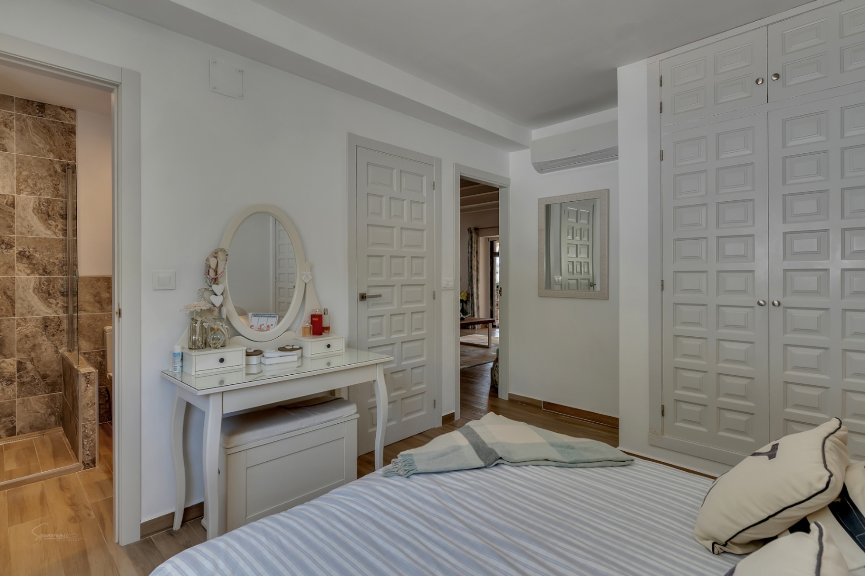 Dormitorio luminoso con tocador blanco, armario empotrado y baño en-suite con azulejos de piedra.