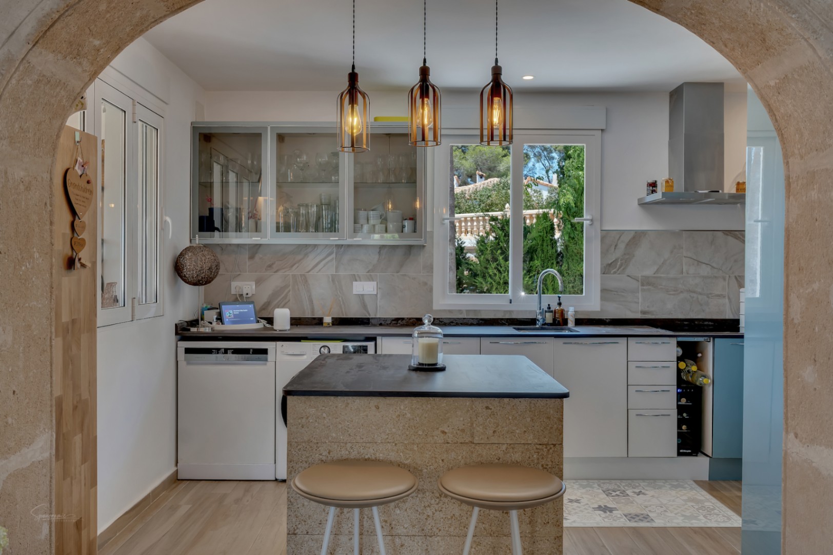 Vista de la cocina moderna con isla central de piedra y lámparas colgantes de diseño.