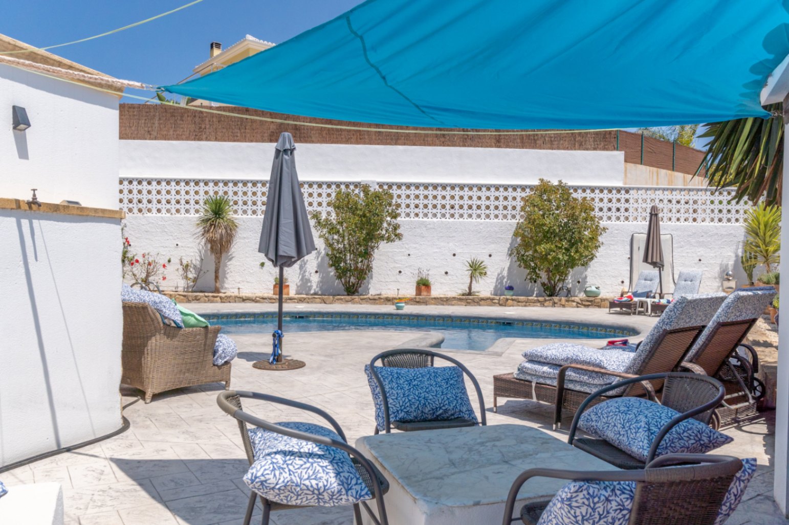 Vista de la piscina con toldo azul y mobiliario de jardín en villa de Jávea.