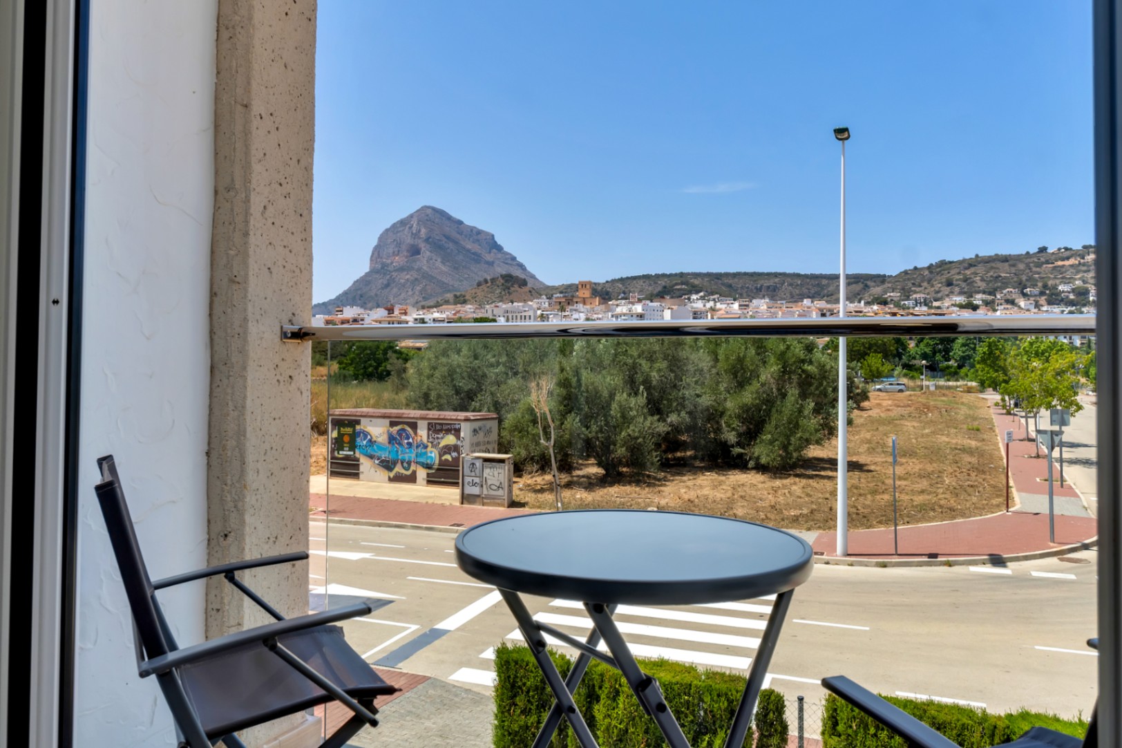 Balcón con barandilla de cristal y mobiliario exterior que ofrece vistas despejadas al Montgó y al casco antiguo de Jávea.