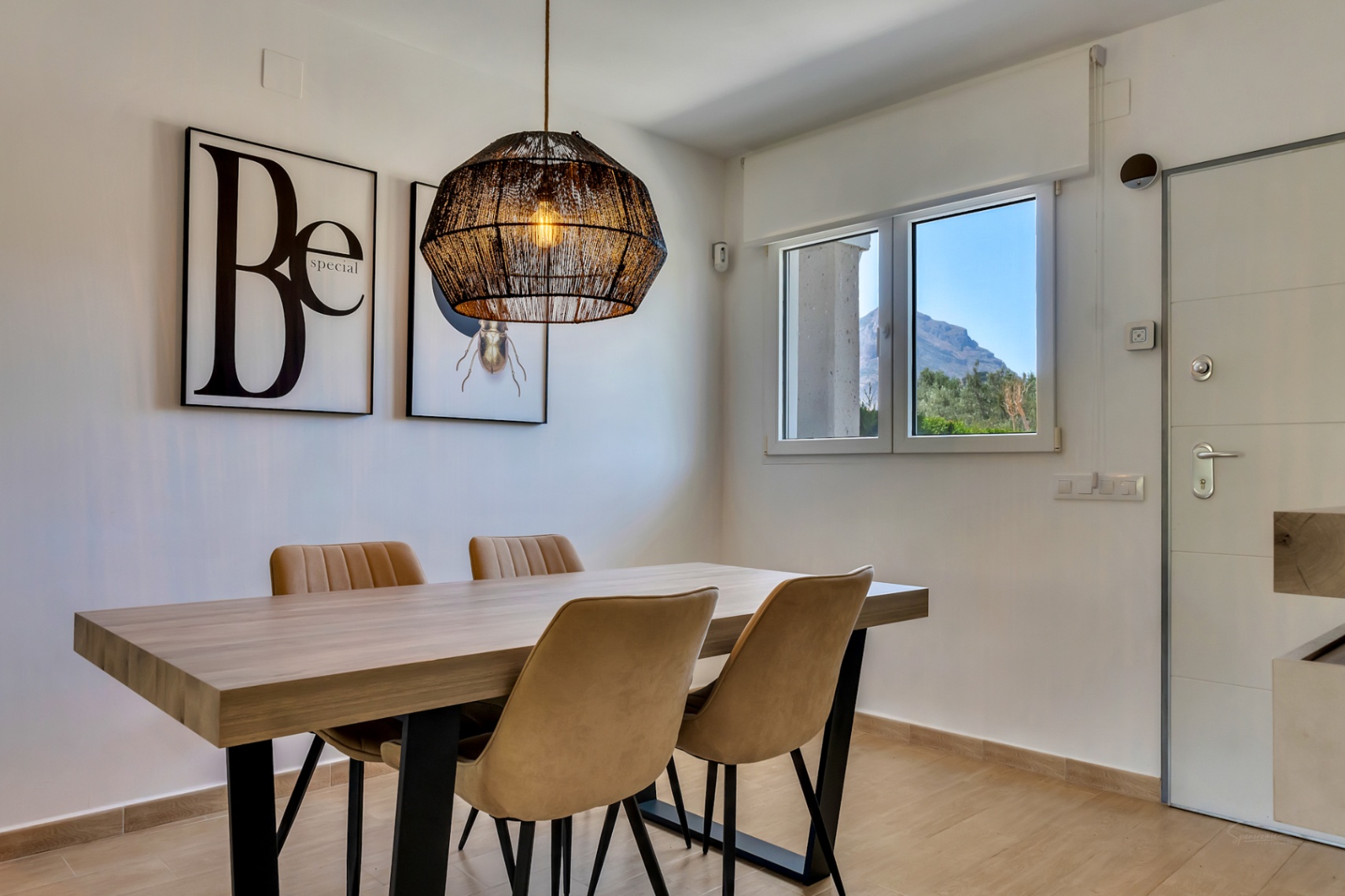 Comedor contemporáneo con mesa de madera, lámpara de fibras naturales y ventana con vistas directas al macizo del Montgó.