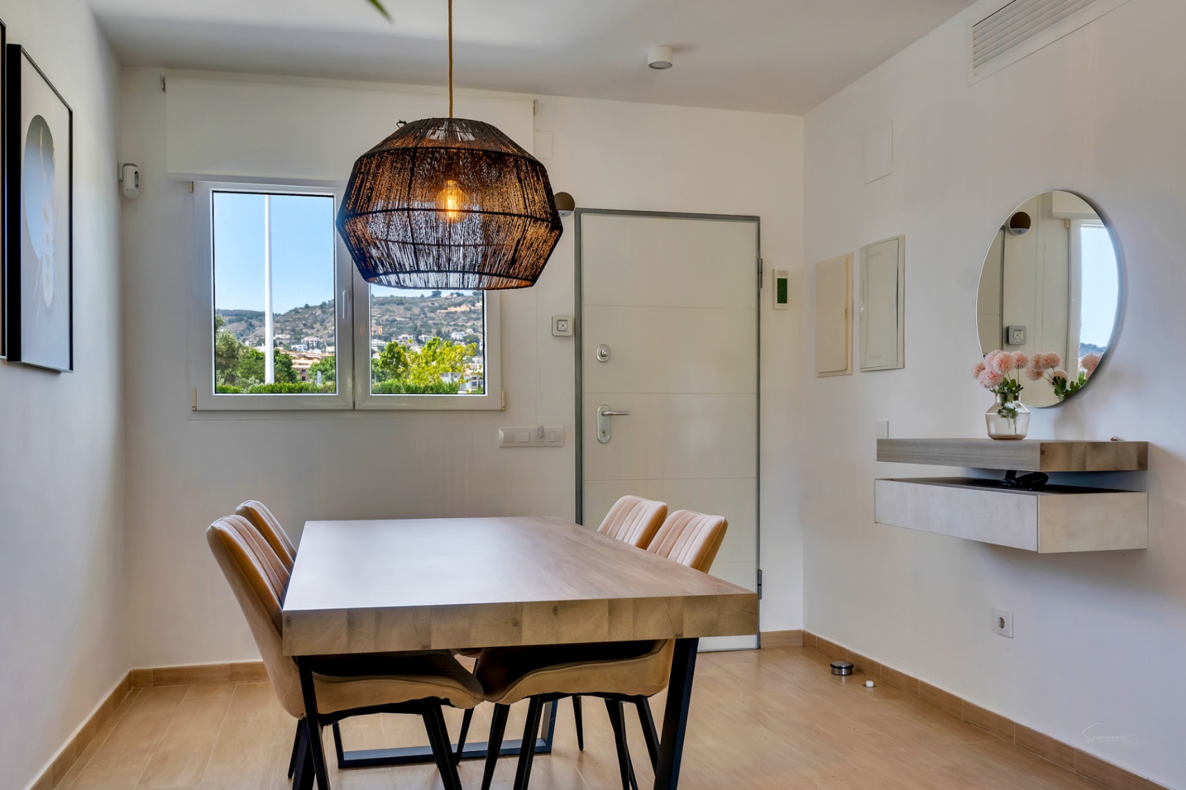 Comedor luminoso con mesa de madera maciza, lámpara de fibras naturales y vistas despejadas. Incluye una consola flotante de diseño y espejo circular.