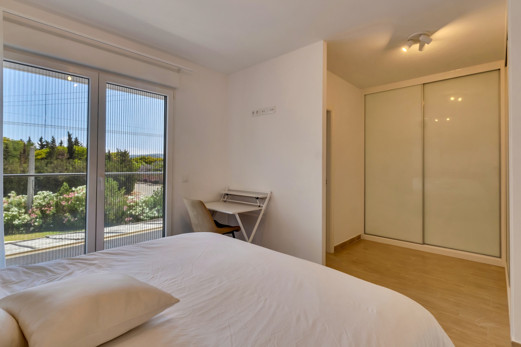 Dormitorio luminoso con armario empotrado de puertas correderas, zona de escritorio y acceso directo a un balcón con vistas despejadas y mosquitera.