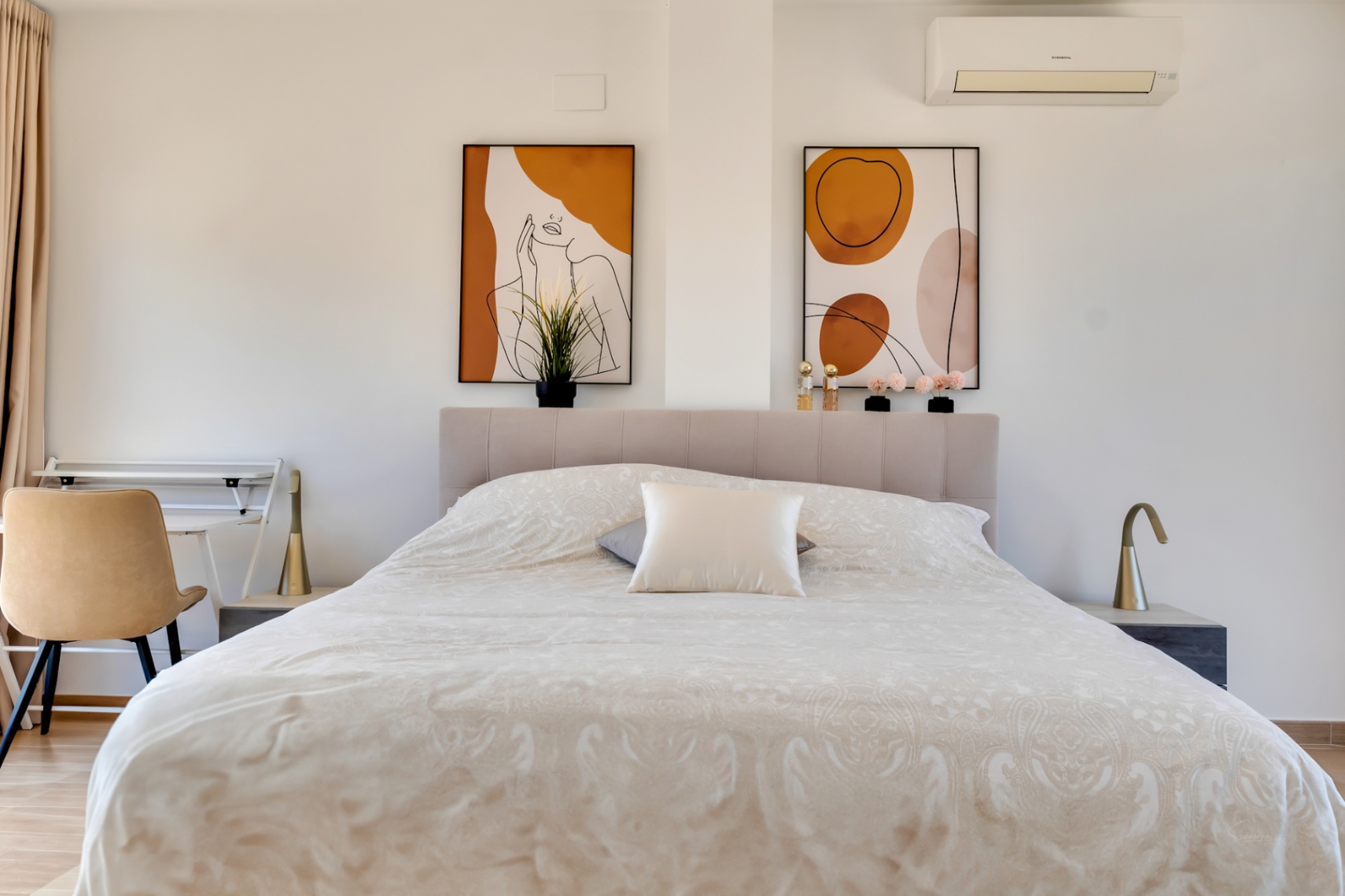 Dormitorio luminoso con cabecero tapizado, arte abstracto en tonos tierra y zona de escritorio integrada. Incluye aire acondicionado y lámparas de diseño minimalista.