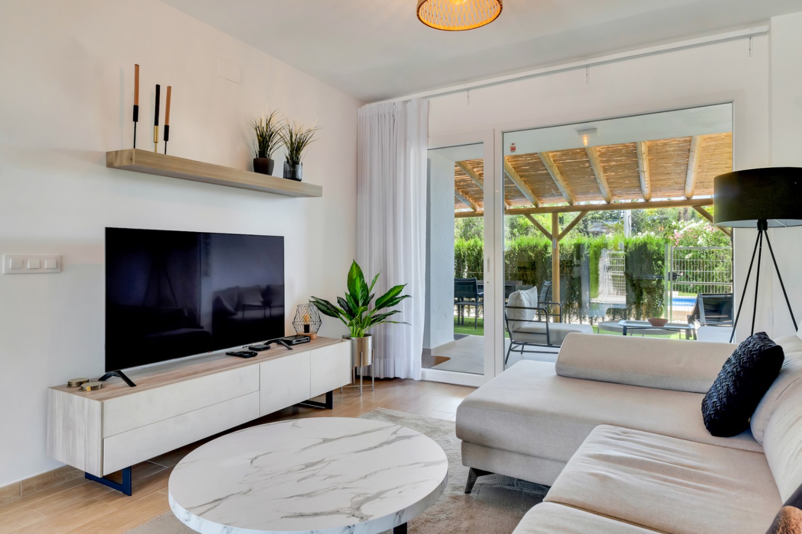 Salón de concepto abierto con mobiliario contemporáneo y acceso directo a través de grandes ventanales al patio privado con pérgola de madera.