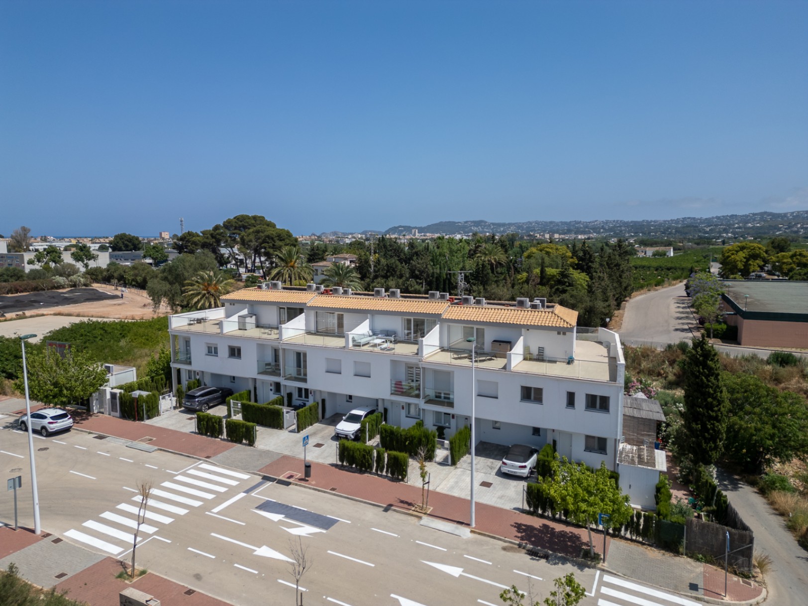 Vista aérea de la fachada principal del complejo residencial moderno, destacando las plazas de aparcamiento privadas y las amplias terrazas superiores con barandillas de cristal.