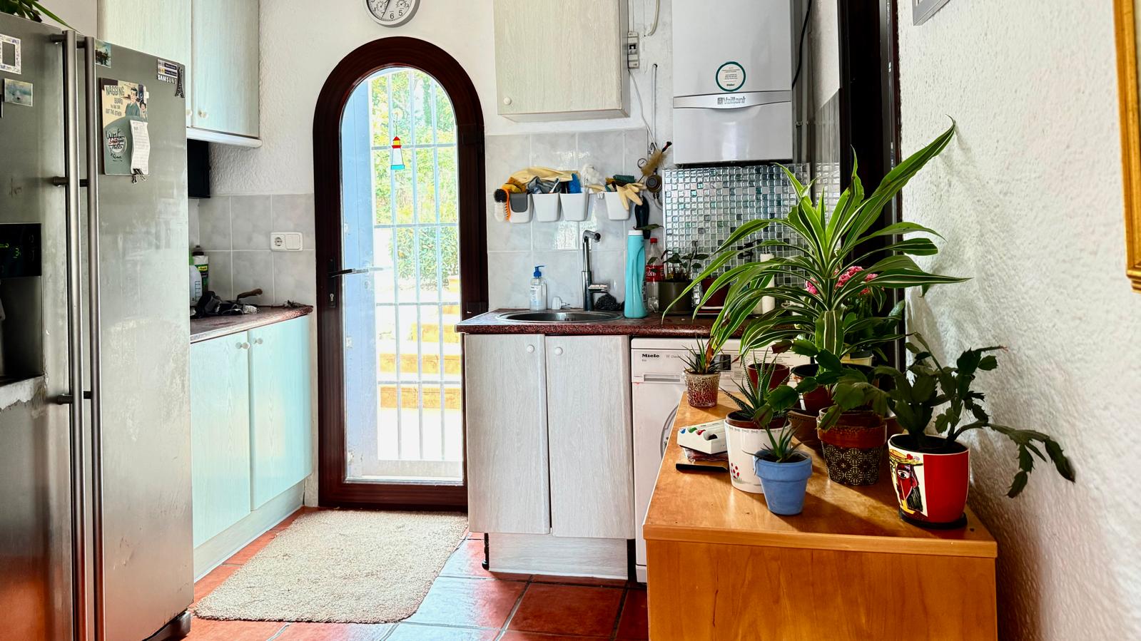Cocina funcional con encimeras de granito, muebles blancos y una puerta de arco acristalada que aporta luz natural y comunica con las terrazas exteriores.