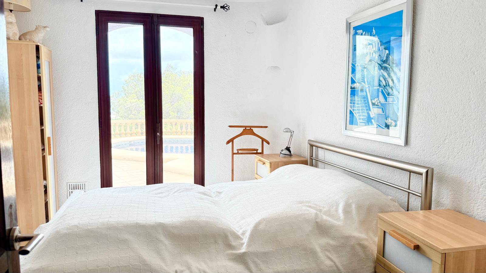 Dormitorio con acceso directo a la terraza de la piscina, paredes blancas texturizadas, mobiliario de madera y vistas al exterior a través de puertas acristaladas.