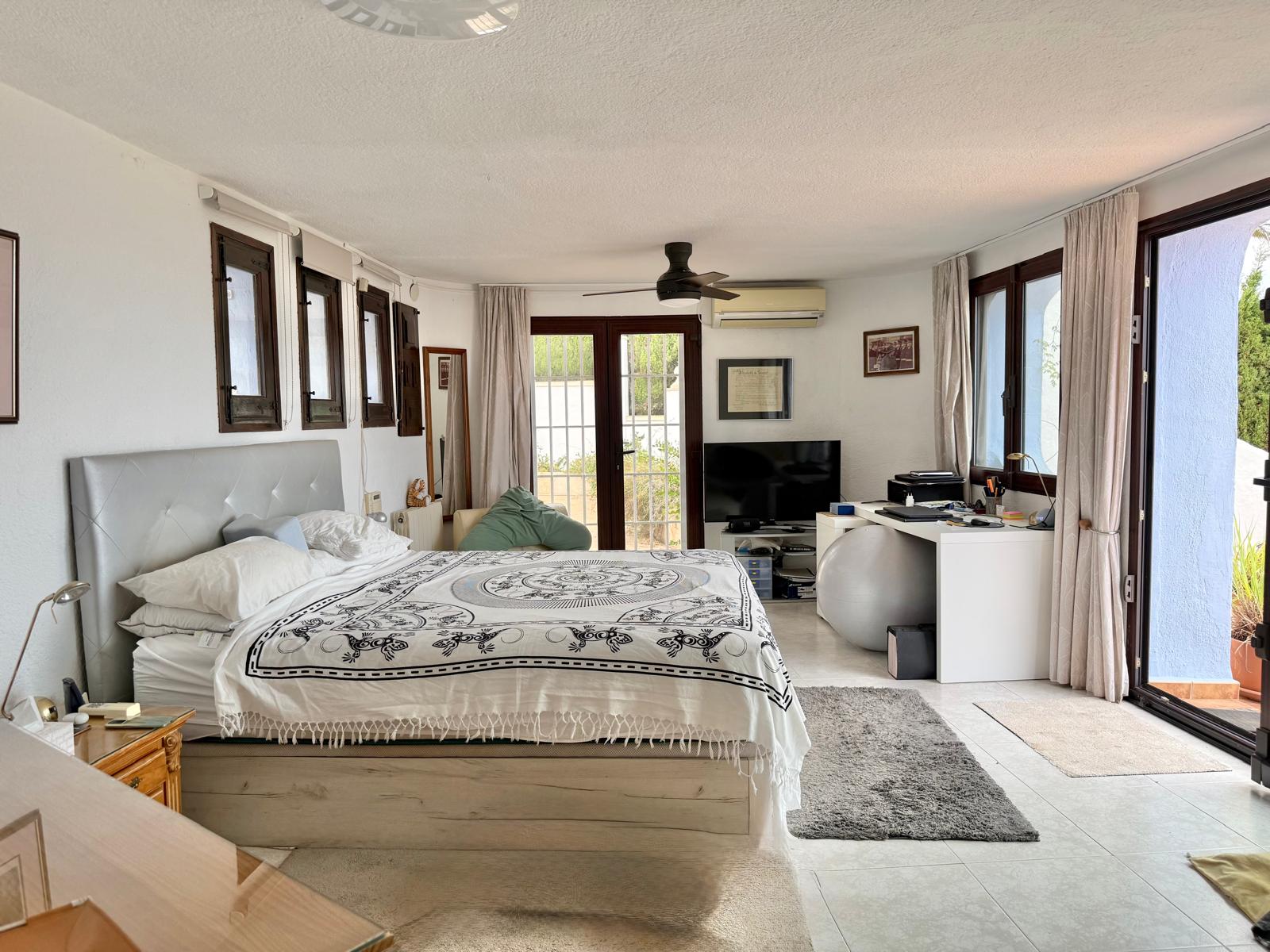 Dormitorio principal amplio con acceso directo a la terraza, zona de despacho integrada, aire acondicionado, ventilador de techo y carpintería de madera oscura.