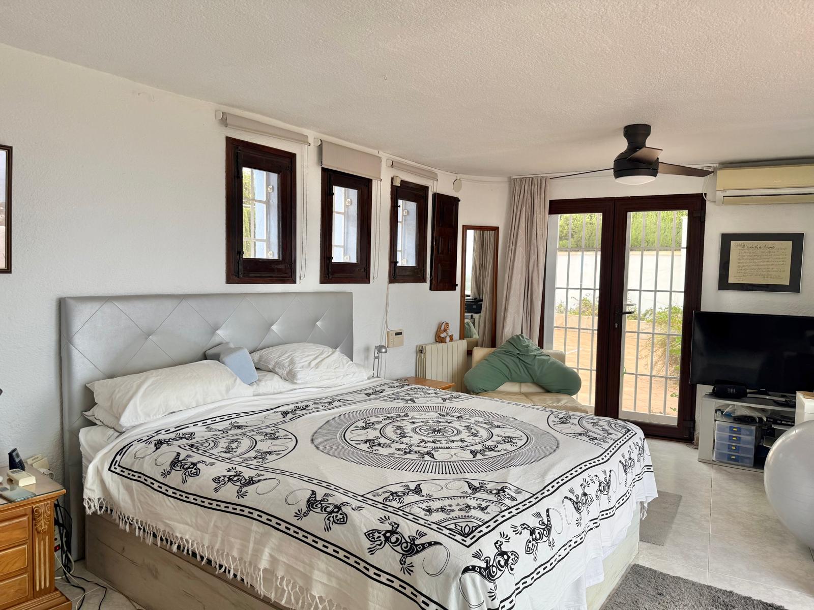 Dormitorio principal luminoso con carpintería de madera oscura, ventilador de techo y puertas acristaladas que conectan directamente con el exterior.