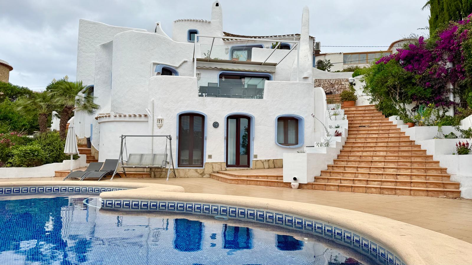 Fachada de estilo ibicenco con formas orgánicas y niveles aterrazados conectados por escaleras exteriores junto a la piscina y el jardín mediterráneo.