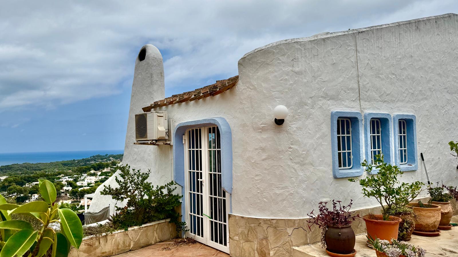 Fachada de estilo ibicenco con muros blancos redondeados, carpintería azul y vistas panorámicas al mar Mediterráneo desde la terraza superior.