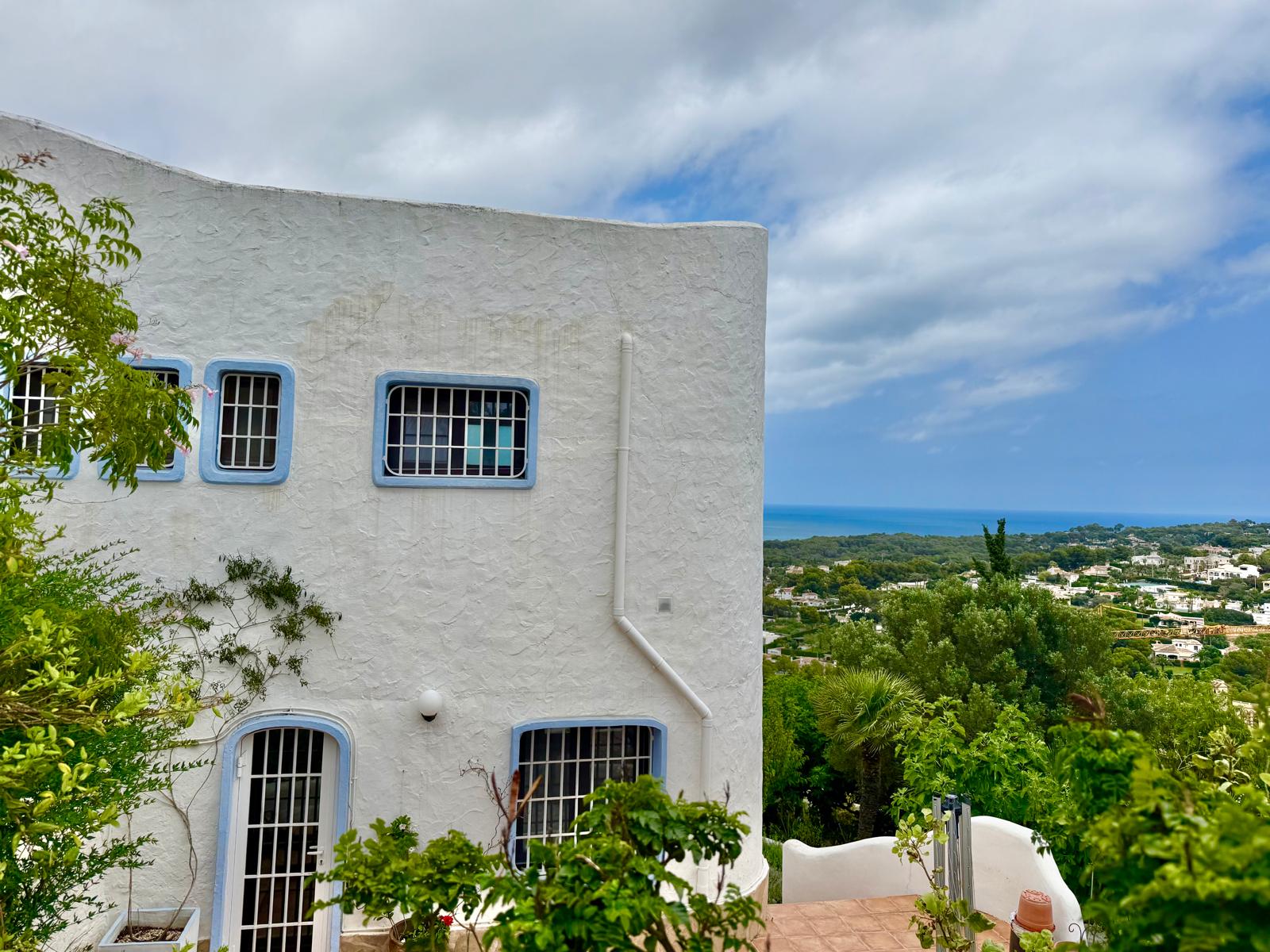 Fachada de estilo ibicenco con muros blancos y marcos azules, ofreciendo vistas panorámicas al mar Mediterráneo y al entorno natural de Jávea.