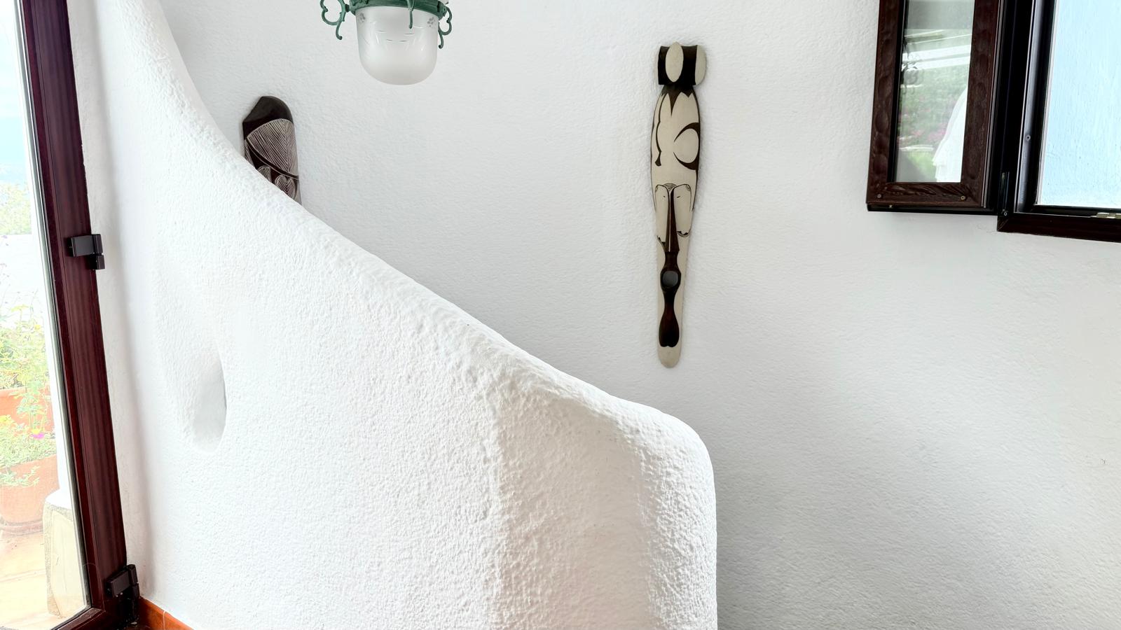 La escalera interior presenta un diseño curvo y orgánico con paredes de acabado rugoso en blanco, complementadas por carpintería de madera oscura.