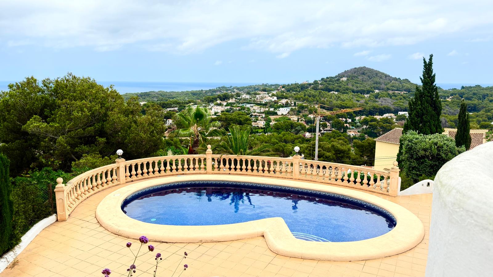 Piscina de diseño curvo rodeada por una terraza de baldosas y balaustrada clásica, con vistas panorámicas al mar Mediterráneo y el paisaje de Jávea.