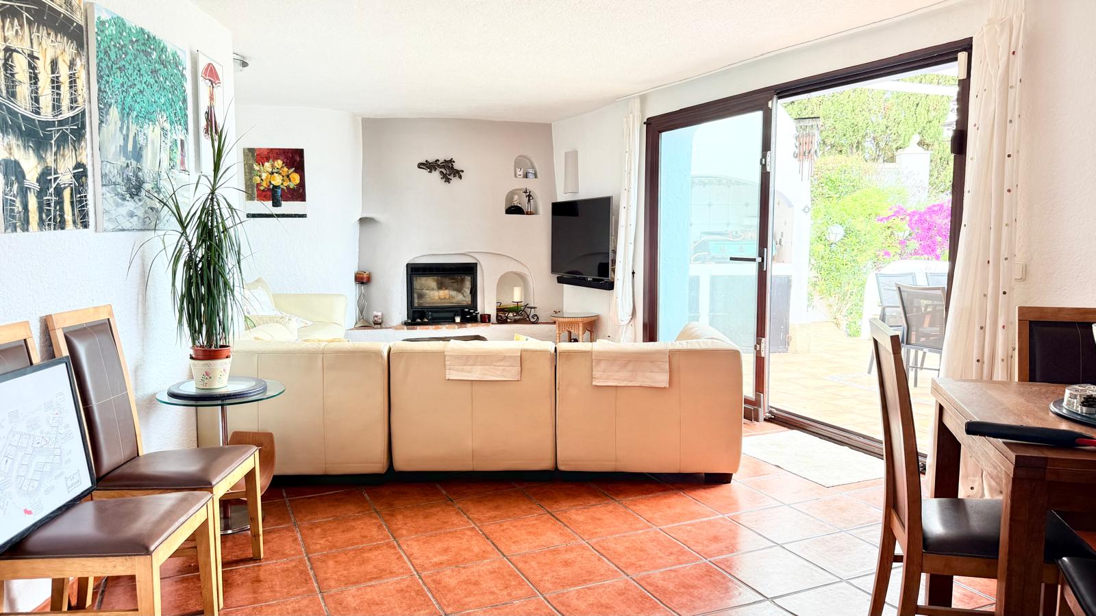 Salón-comedor con suelos de terracota, chimenea de leña encastrada y acceso directo a la terraza a través de grandes ventanales correderos.