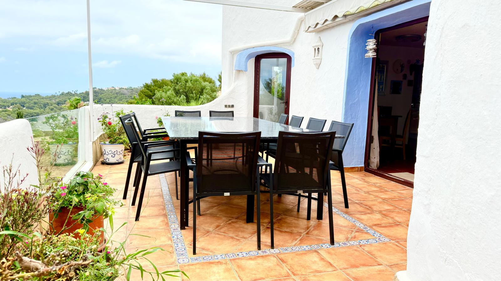 Terraza comedor exterior con mesa de granito, suelos de terracota con cenefas cerámicas y vistas panorámicas al entorno natural de Jávea.