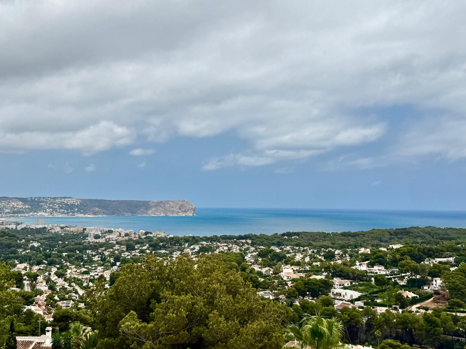 Vistas panorámicas elevadas hacia la bahía de Jávea y el cabo de San Antonio, con el mar Mediterráneo y el entorno residencial rodeado de vegetación.