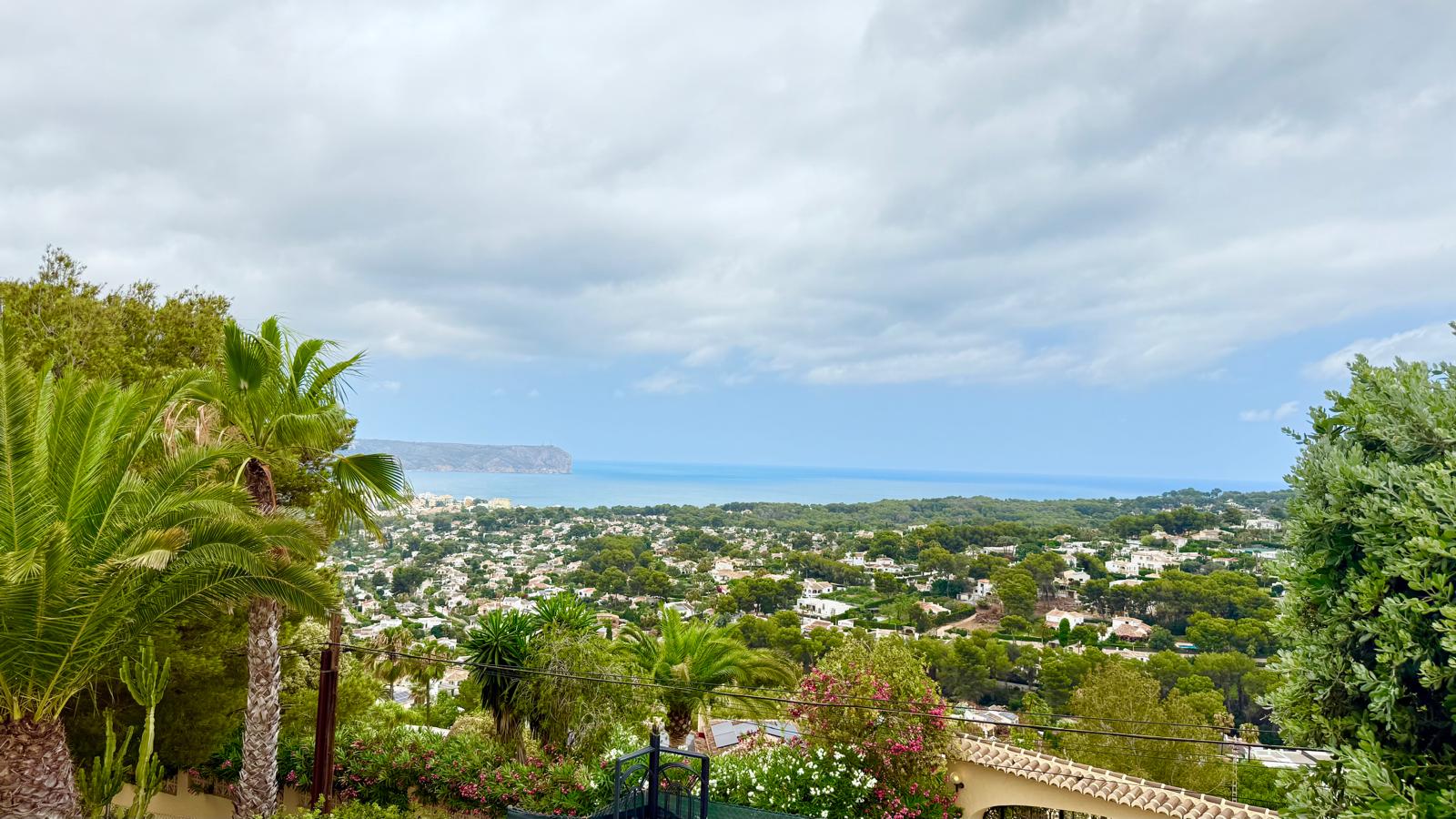 Vistas panorámicas hacia la bahía de Jávea y el mar Mediterráneo desde la posición elevada de la villa, rodeada de palmeras y vegetación madura.