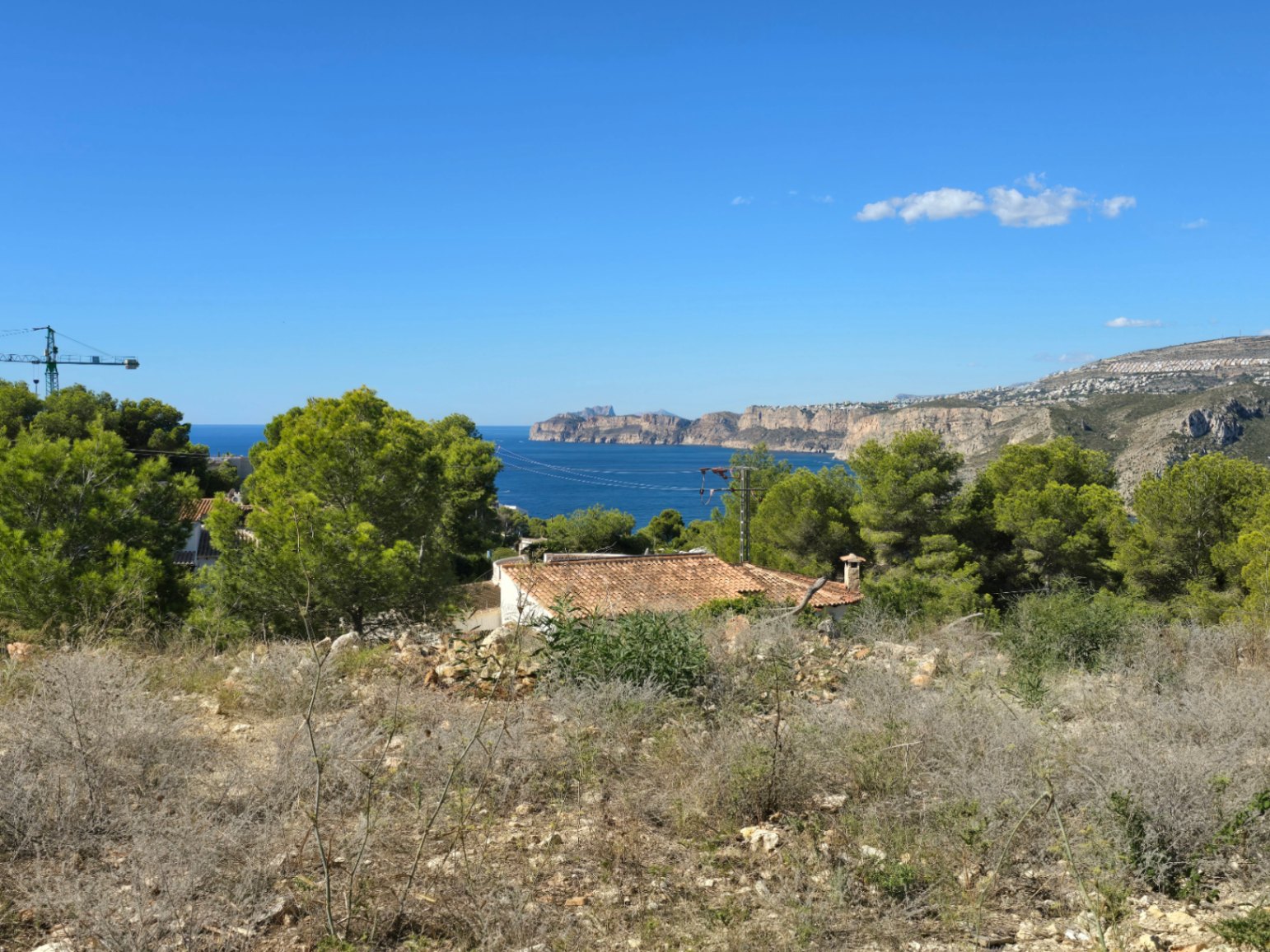 Vista panorámica al mar Mediterráneo y los acantilados costeros desde la parcela elevada, rodeada de pinos y vegetación autóctona en Jávea.