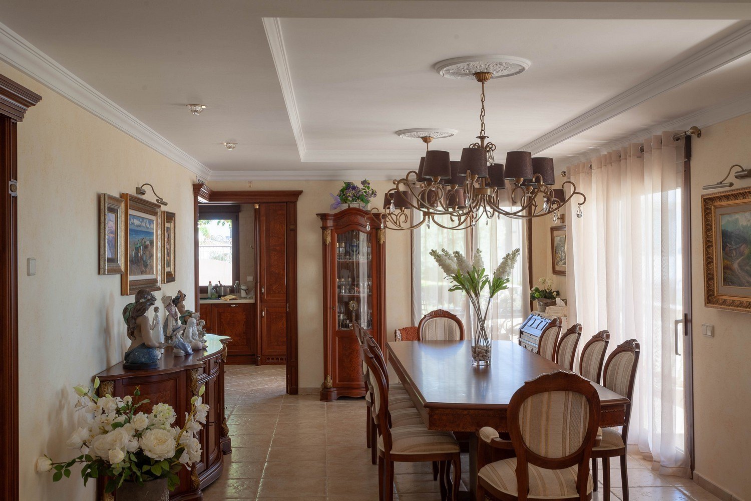 Comedor clásico con mesa de madera, lámpara de araña y vitrina de madera con detalles dorados.