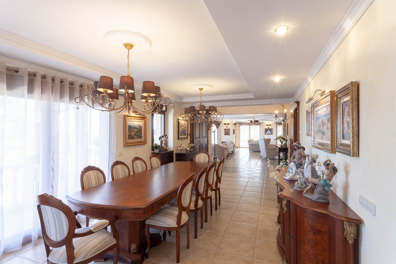 Comedor elegante con mesa de madera oscura, sillas tapizadas y lámparas de araña clásicas.