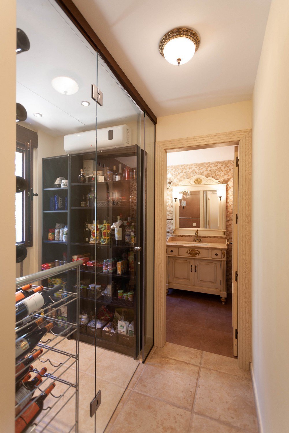 Detalle de despensa con puerta de cristal y baño con tocador clásico.