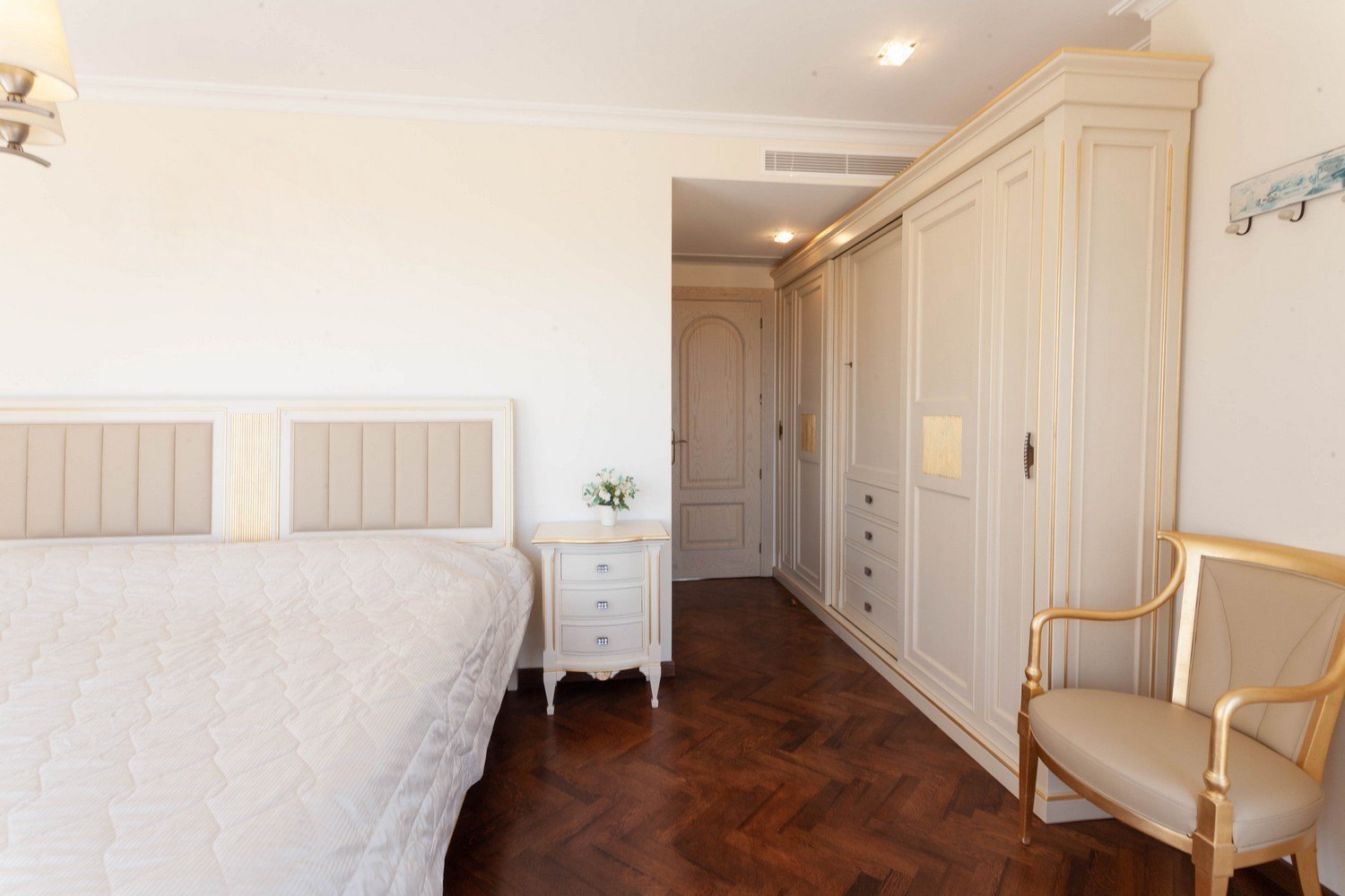 Dormitorio con cama de cabecero tapizado, armario empotrado de madera clara y suelo de parquet oscuro.