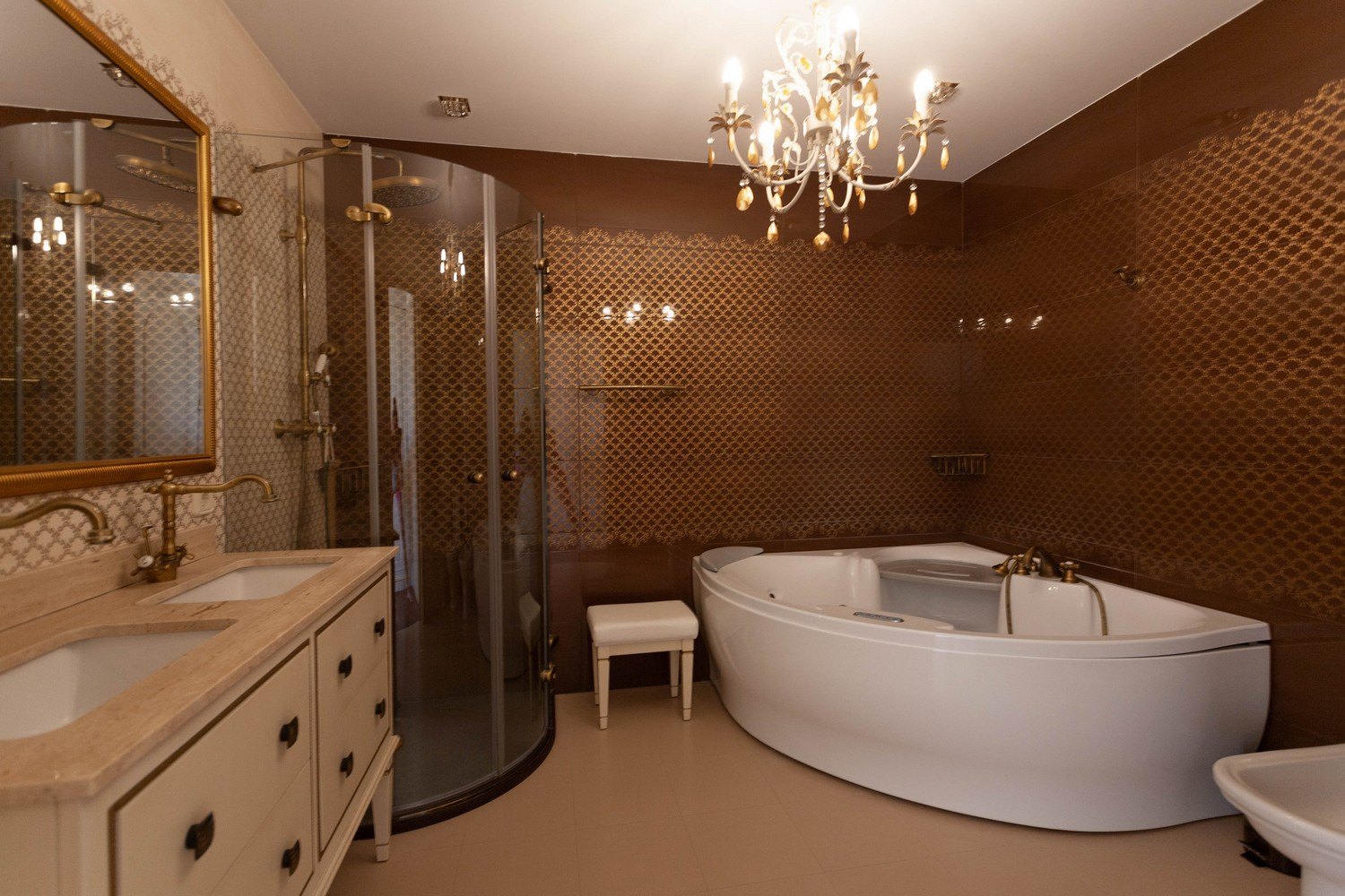 Elegante baño con bañera de hidromasaje, ducha con mampara curva y lavabo doble con grifería dorada.
