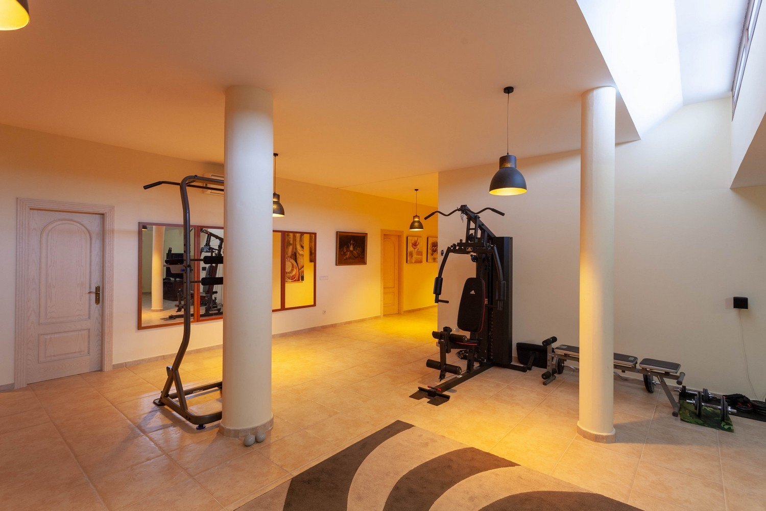 Gimnasio luminoso con suelo de baldosas, equipado con máquinas de ejercicios y luz natural cenital.
