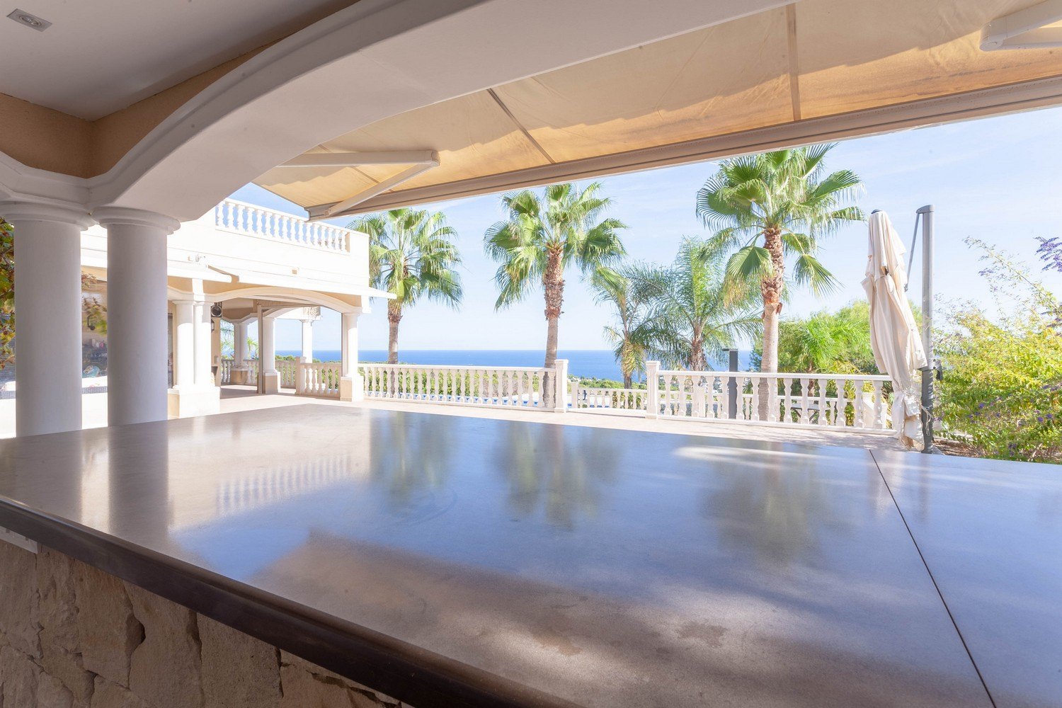 Terraza cubierta con barra de piedra y vistas al mar y palmeras en urbanización Raco de Galeno, Benissa.
