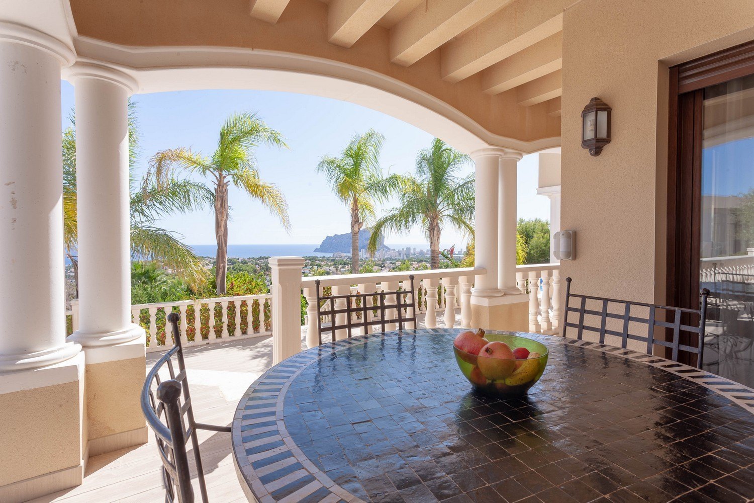 Terraza cubierta con mesa de mosaico y vistas panorámicas al mar.