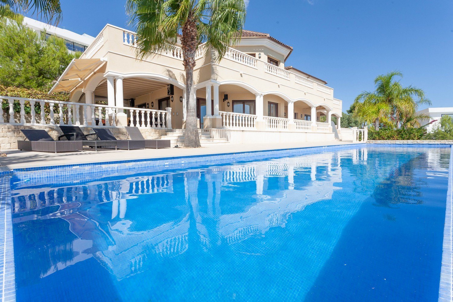 Vista de la piscina "Infinity" con baldosa azul y la fachada de la villa mediterránea con columnas.