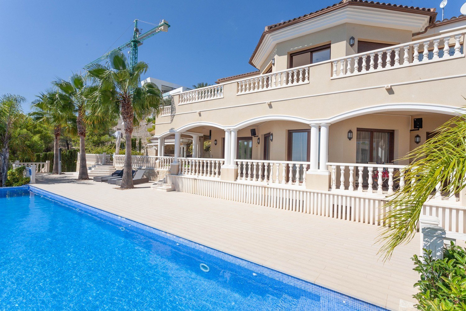 Vista de la piscina y fachada de la villa mediterránea con barandilla de balaustres blancos.