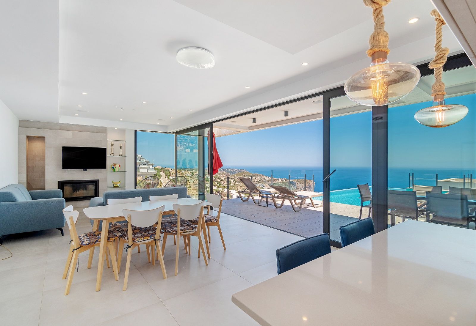 Salón comedor de concepto abierto con amplios ventanales correderos que integran la terraza, la piscina infinita y las vistas panorámicas al mar Mediterráneo.