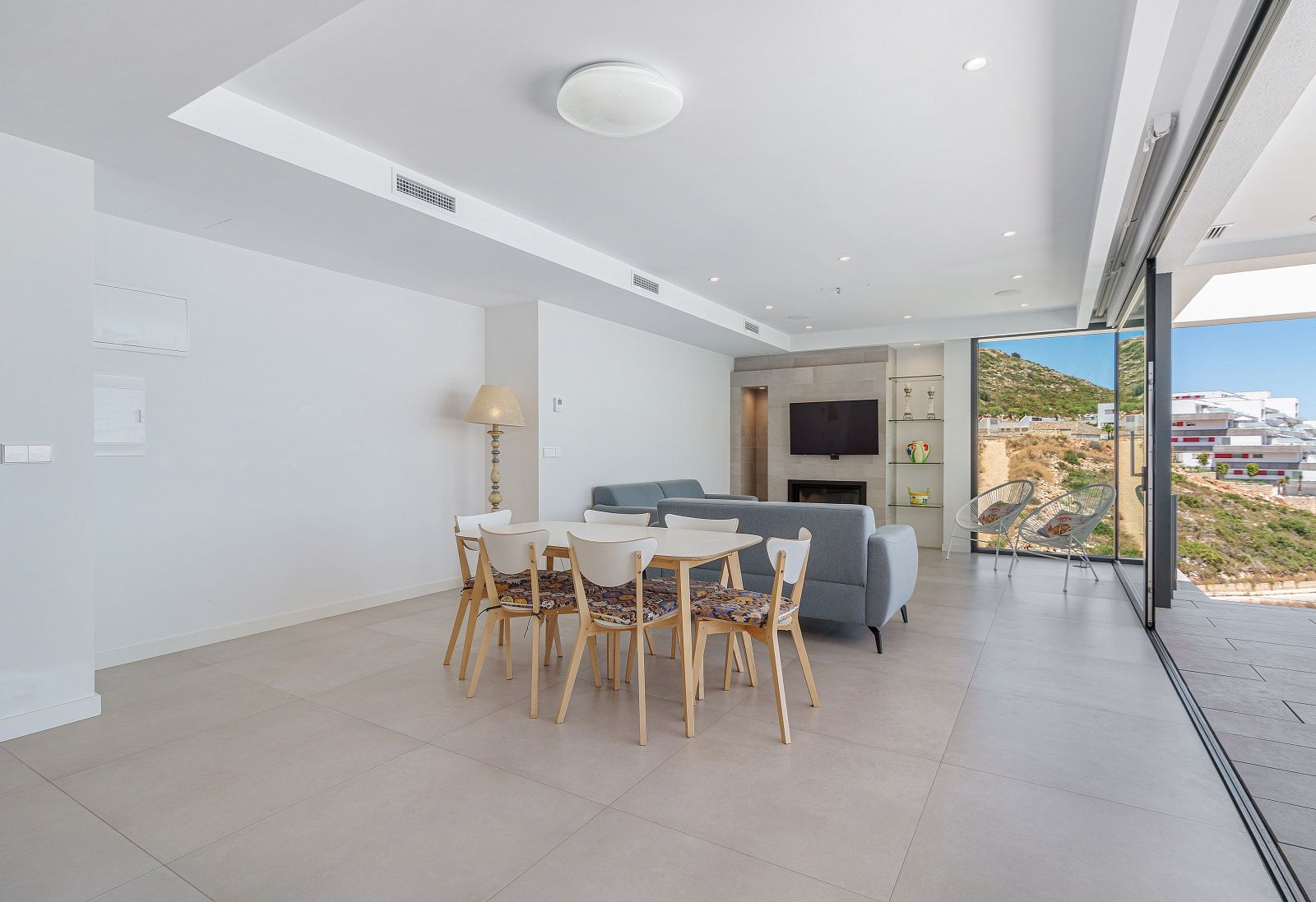Salón comedor diáfano con suelos de gres porcelánico, zona de estar con chimenea integrada y grandes ventanales que ofrecen vistas despejadas al entorno natural.