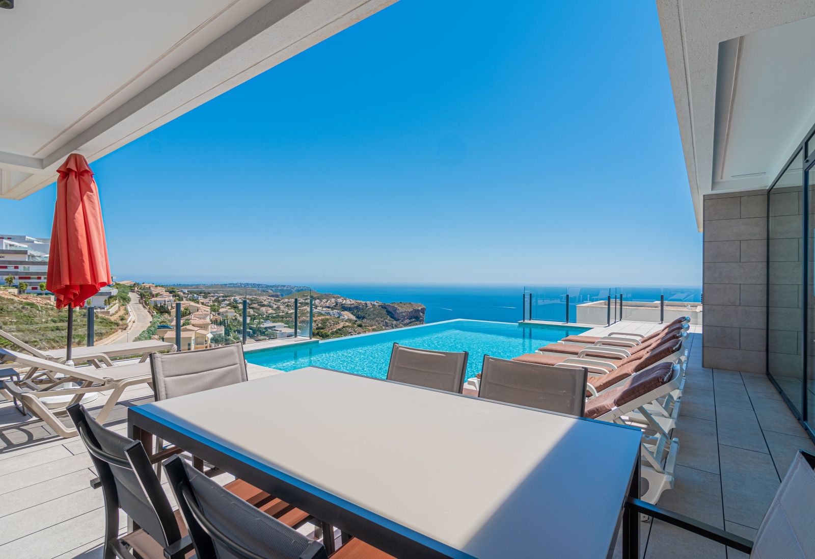 Terraza principal con piscina infinita, zona de comedor exterior y vistas panorámicas al mar Mediterráneo y la costa de Benitachell.