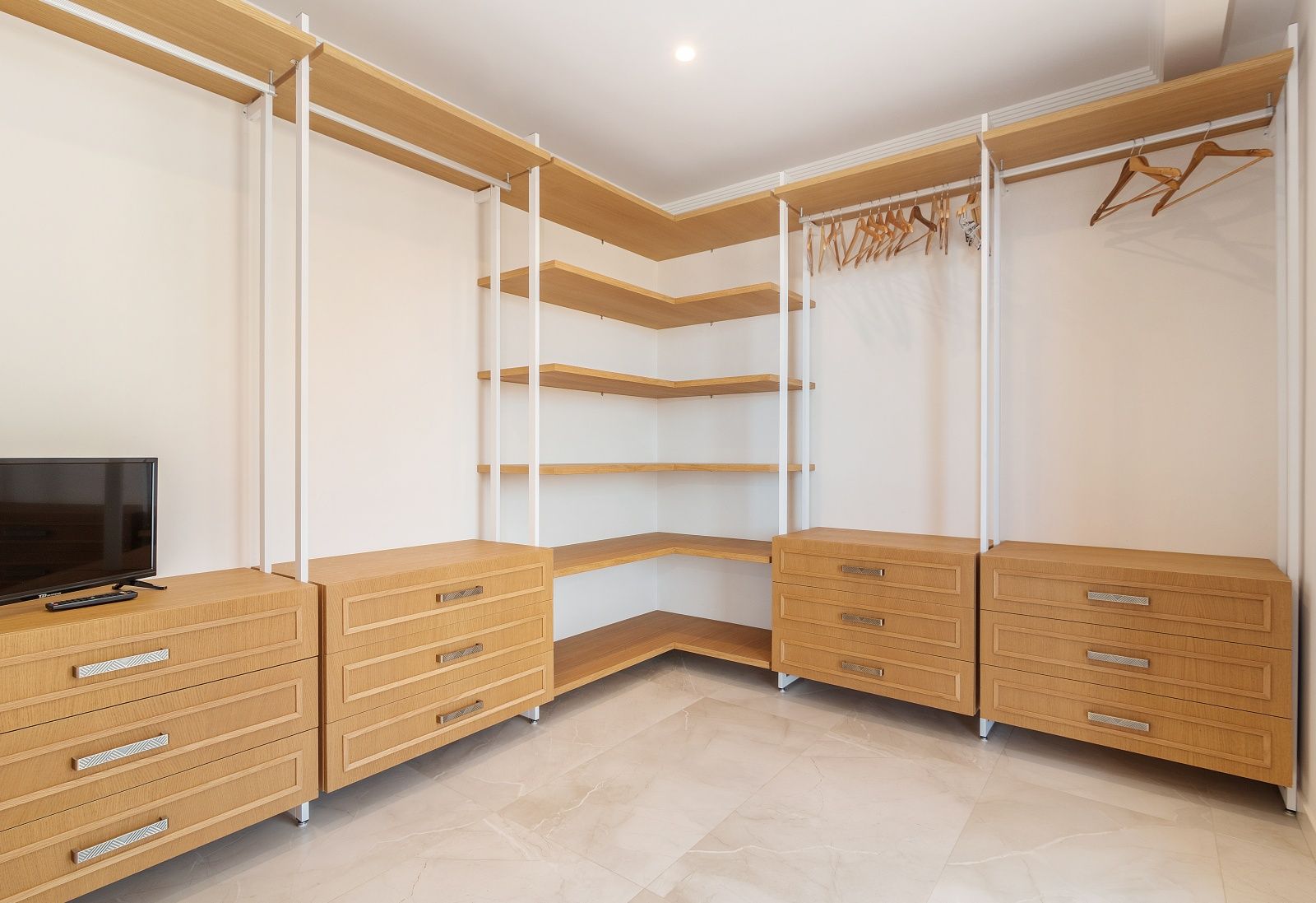 Vestidor abierto con estanterías de madera de roble, cajoneras modulares y suelo de gres porcelánico pulido con efecto mármol.