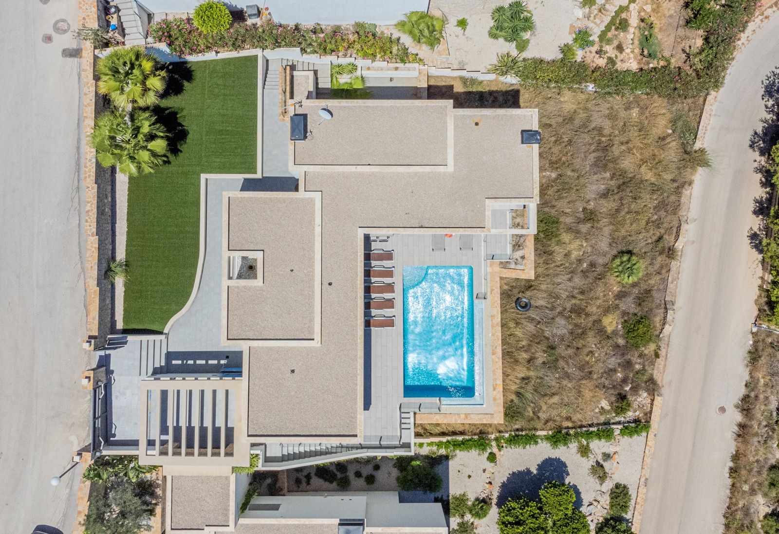 Vista aérea cenital de la villa que muestra la distribución de la parcela, la piscina rectangular con solárium, las cubiertas planas de grava y las zonas ajardinadas.
