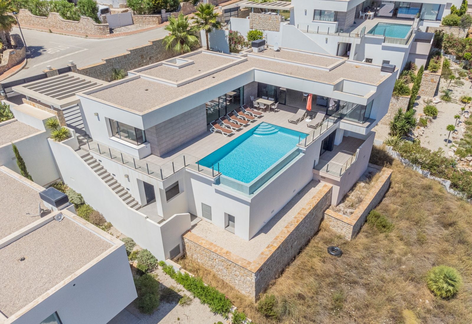 Vista aérea de la villa moderna con piscina infinita de borde de cristal, amplia terraza con tumbonas y arquitectura minimalista de líneas rectas en Cumbre del Sol.