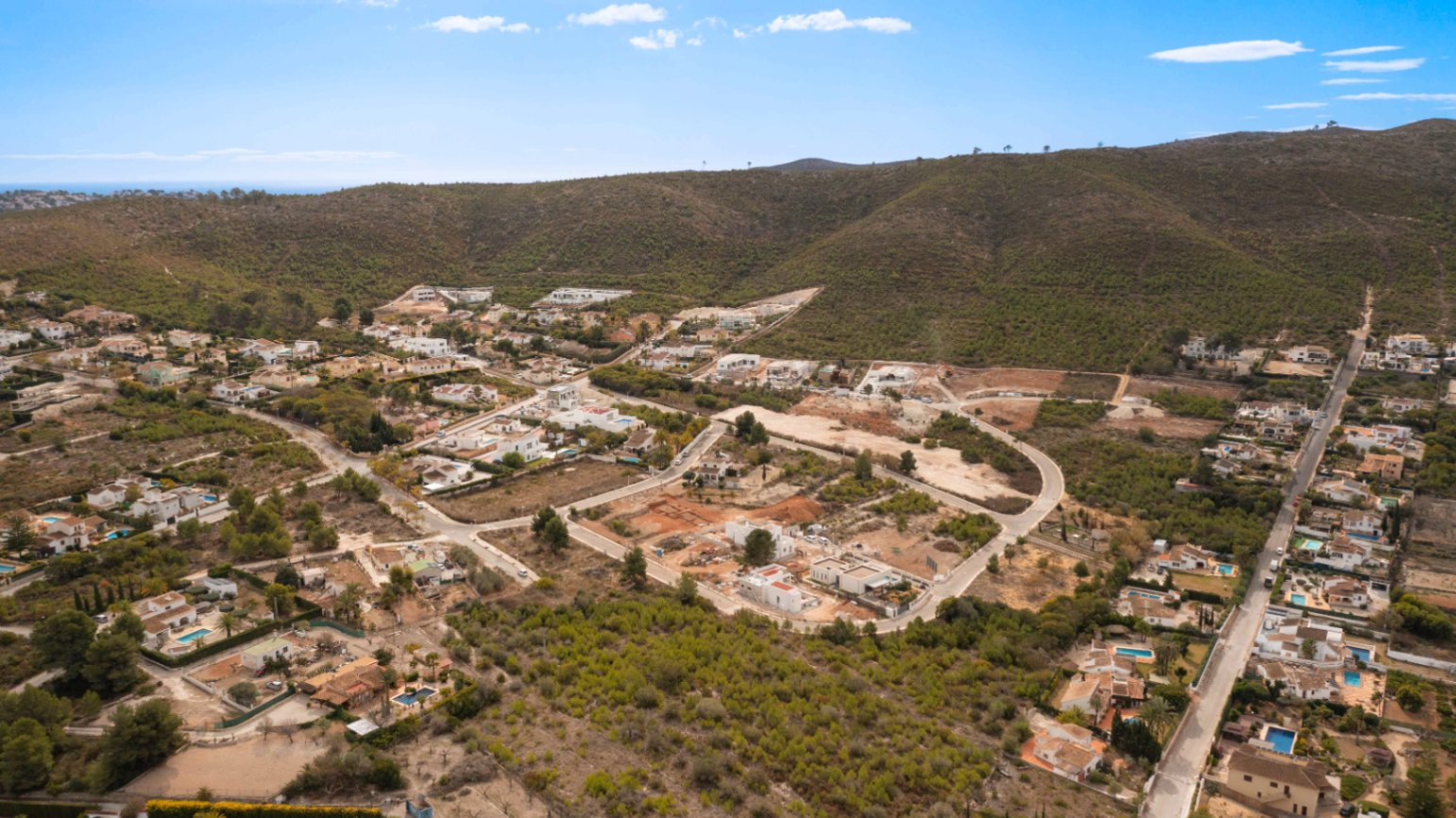 Panorámica aérea de la urbanización Lomas Del Rey en Jávea, destacando la disposición de las parcelas entre colinas de vegetación mediterránea y pinos.