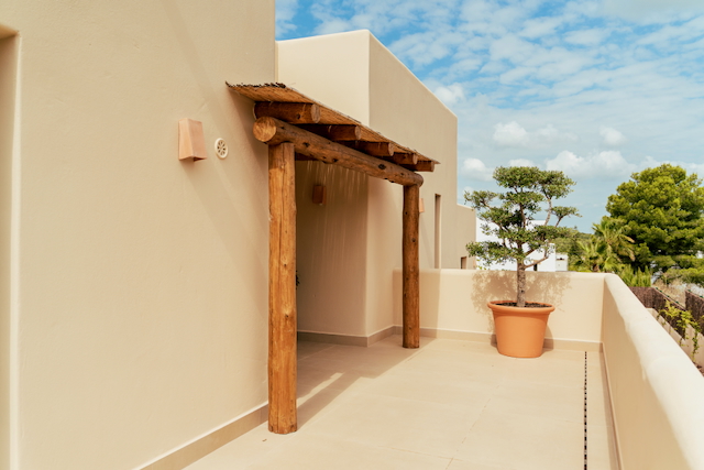 Terraza superior con pérgola de troncos de madera rústica y techo de cañizo, complementada por un árbol ornamental en maceta de terracota sobre suelo cerámico.