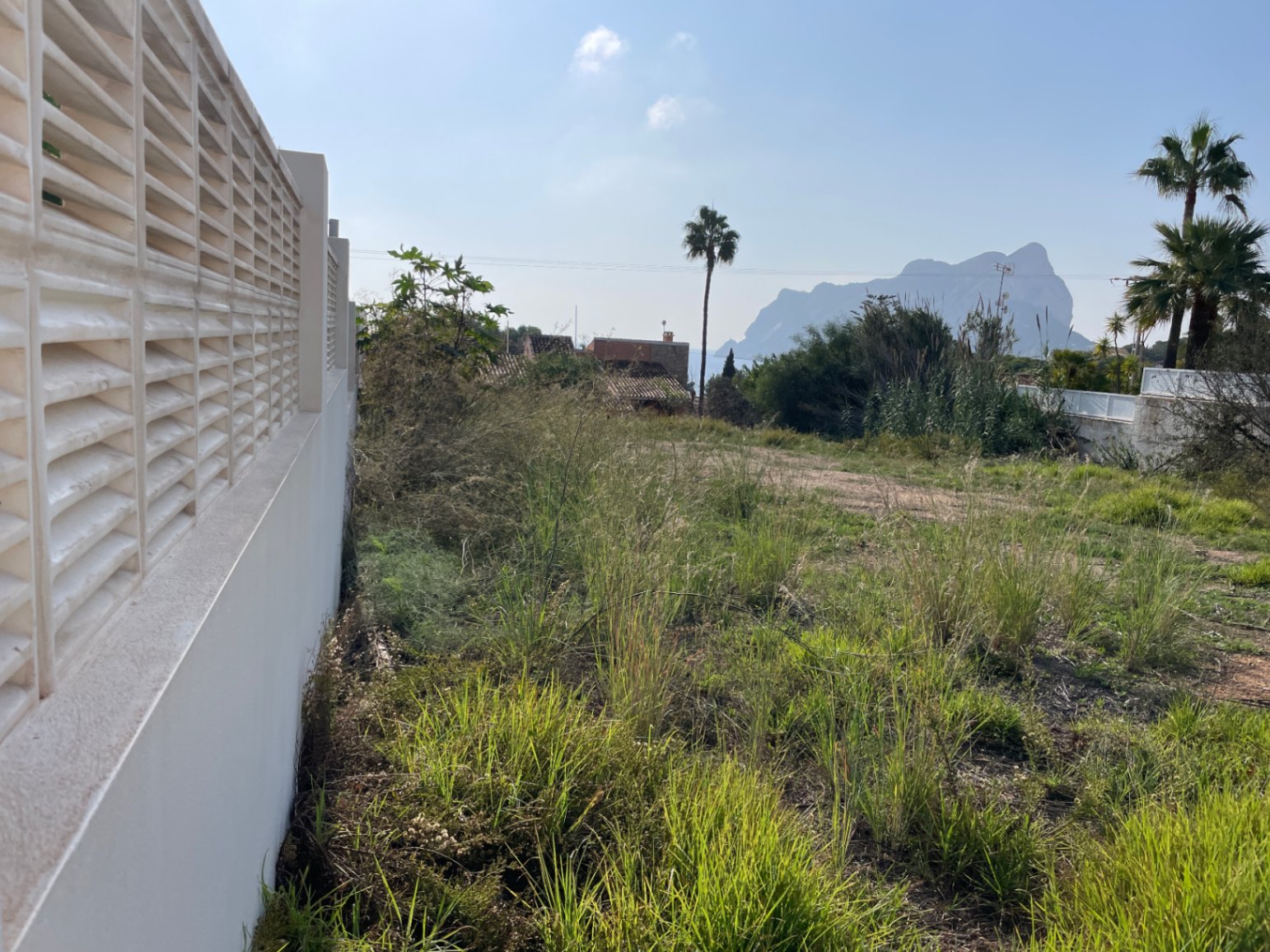 Parcela llana en Bassetes, Calpe, con vistas despejadas al Peñón de Ifach. Incluye muro perimetral con celosía blanca y vegetación natural mediterránea.
